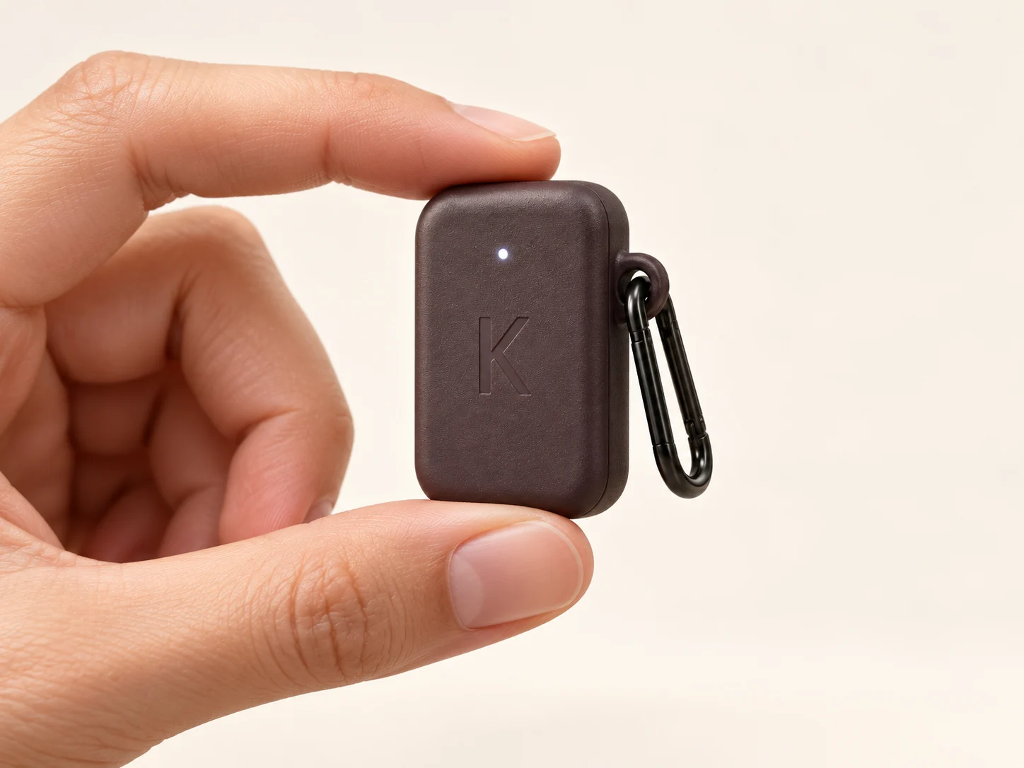 The Kinesis clip held between finger and thumb, its carabiner open at the side, small enough to disappear in a hand.